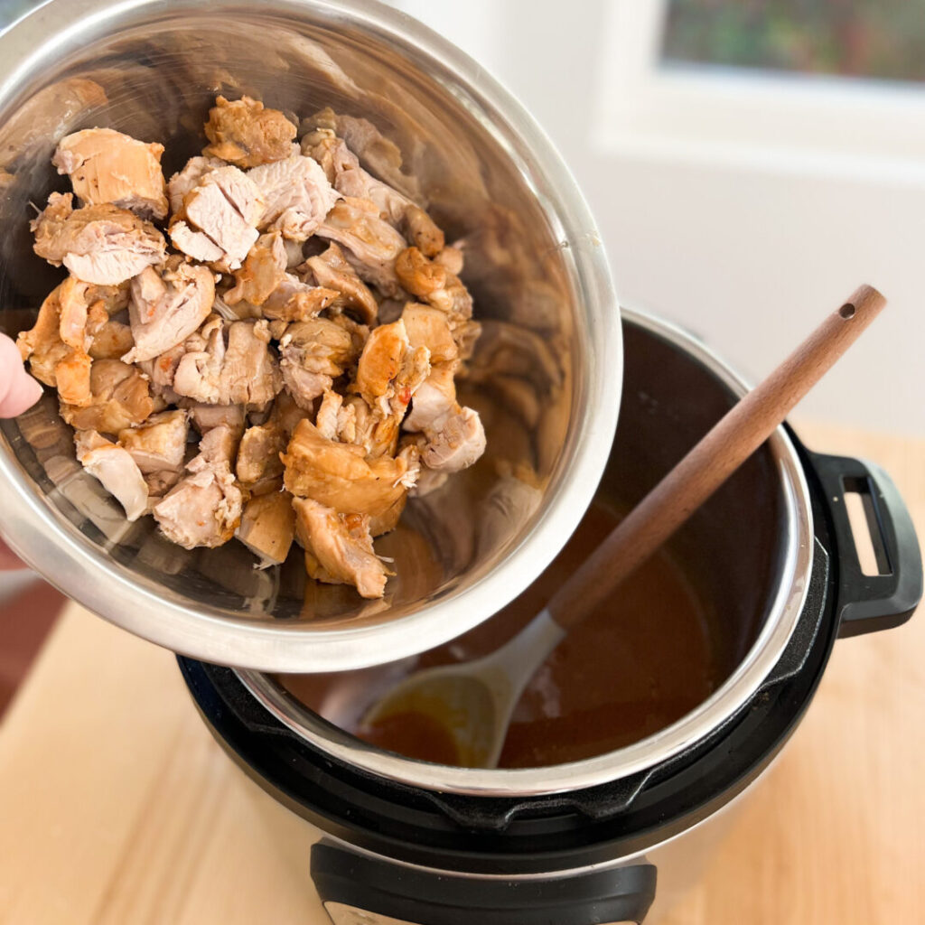 Cut cooked chicken being poured into an Instant Pot.