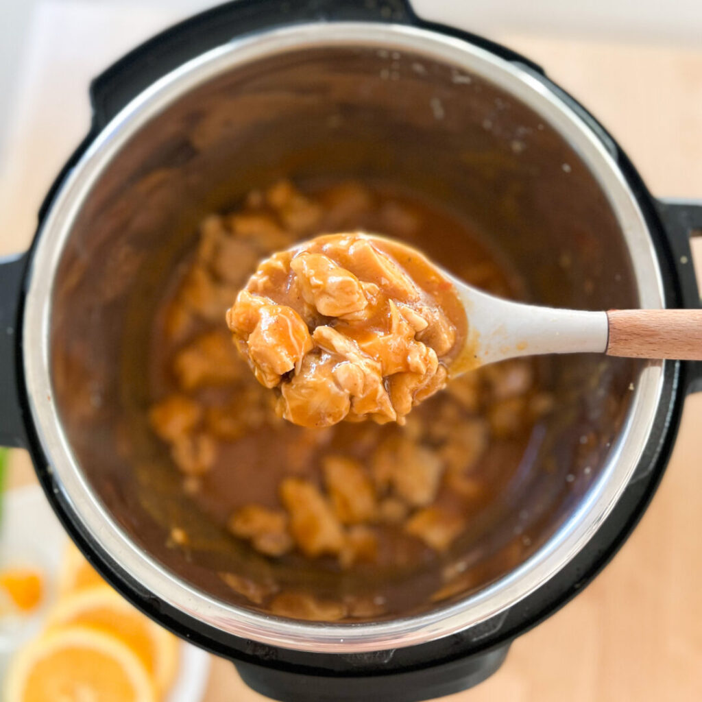 A spoonful of orange chicken over an Instant Pot.